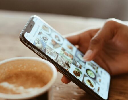 Hand browsing social media photos on a smartphone next to a cup of coffee indoors.