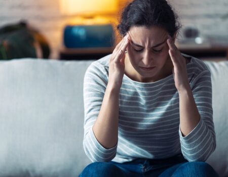 Young woman with headache sitting on the sofa in the living room