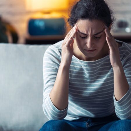 Young woman with headache sitting on the sofa in the living room