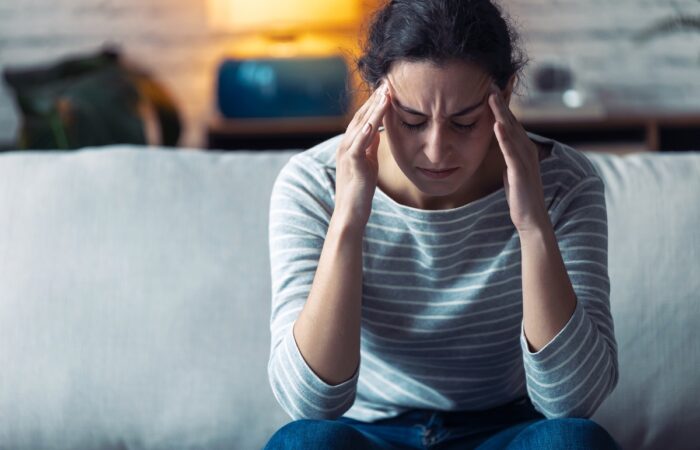 Young woman with headache sitting on the sofa in the living room